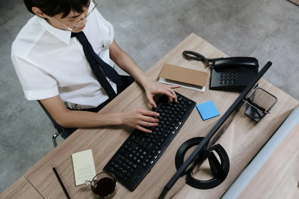 Pria Asia berpakaian bisnis mengetik di keyboard di meja kantor modern